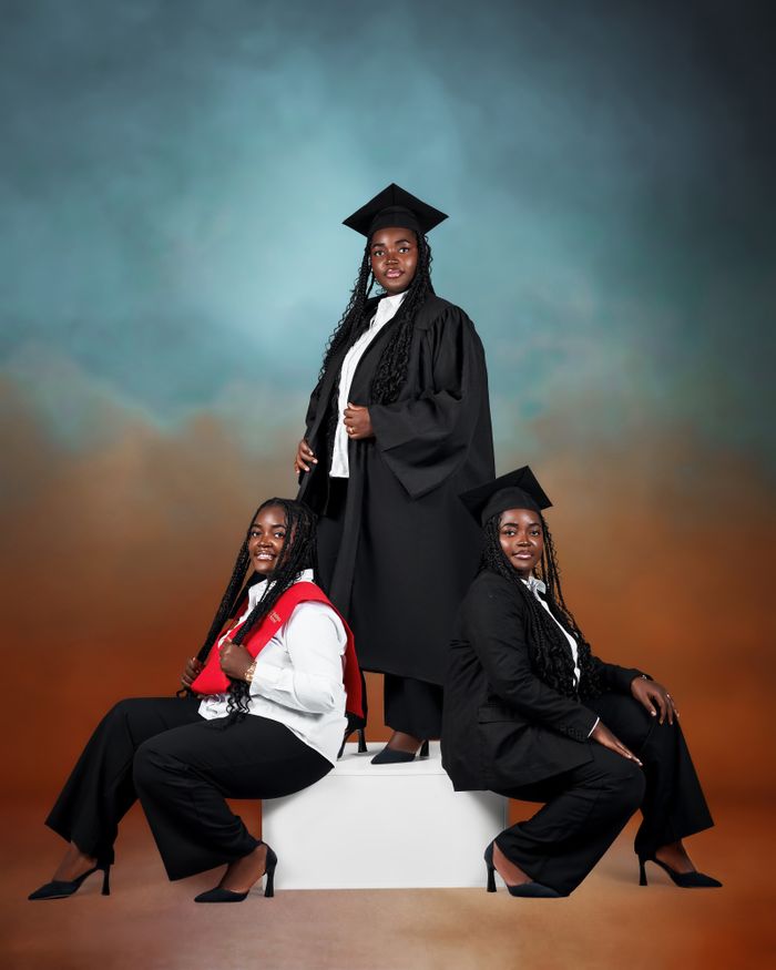 Three female graduates in academic regalia posing confidently on graduation day.
